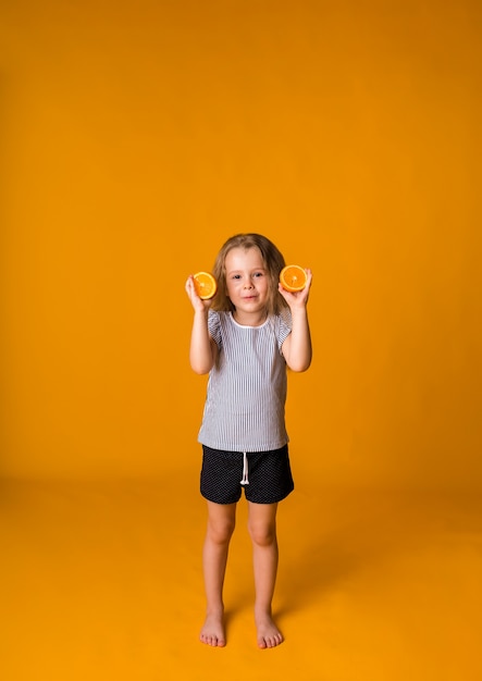 Little girl stands with orange halves on a yellow surface with space for text