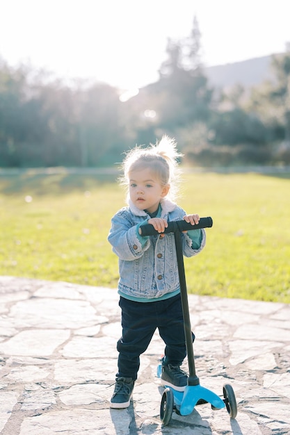 Little girl stands with a scooter on a path in the park