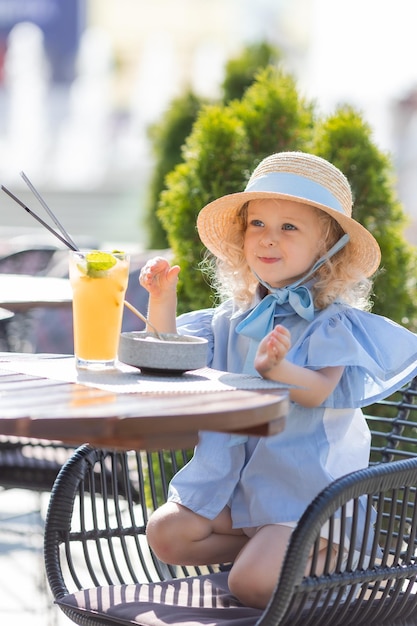 La bambina con un cappello di paglia e un vestito blu sta facendo colazione all'aperto