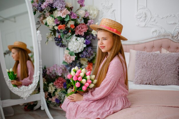 A little girl in a straw hat holds a bouquet of spring flowers at home