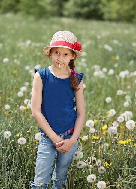 緑の牧草地に立っているわらの帽子をかぶった少女