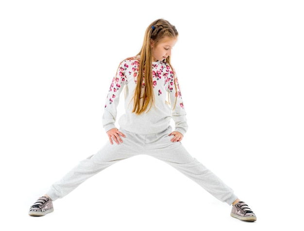 어린 소녀는 흰색 배경에 격리된 회색 패션 스포츠웨어를 입고 스트레칭 운동을 합니다.