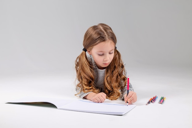 Little girl in a striped dress draws in an album lying on the floor child development lifestyle