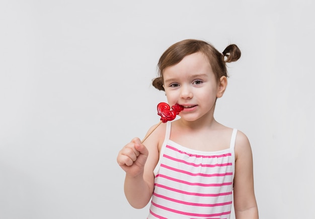 ロリポップの縞模様のドレスの少女。オンドリの形をした棒のロリポップ。子供のための甘い