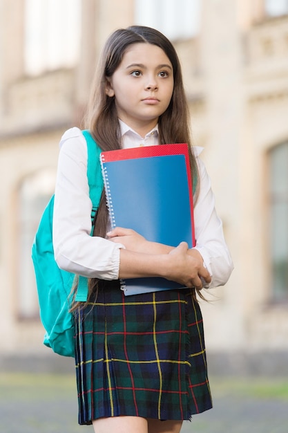 小さな女の子の学生服とバックパックは、本の学年の概念を保持します