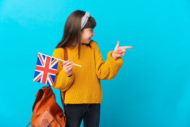 Little girl studying english isolated on blue background pointing finger to the side and presenting a product