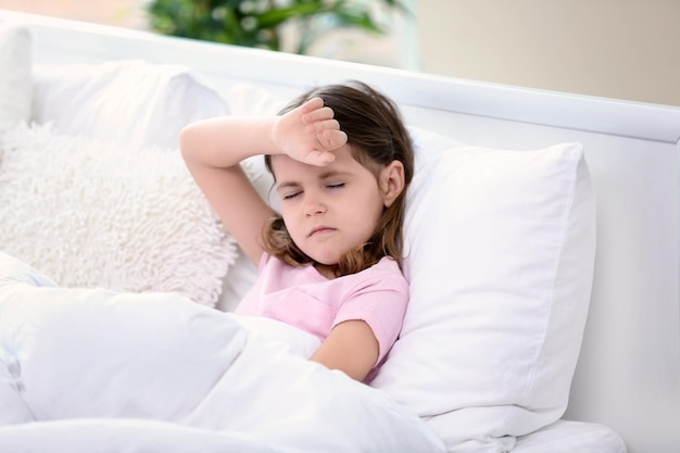 little girl suffering from headache while lying in bed at home