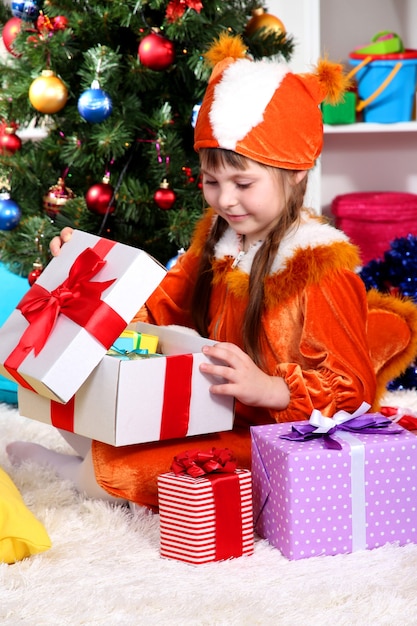 Little girl in suit of squirrels opens gift in festively decorated room