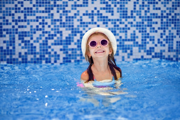 Маленькая девочка в солнцезащитные очки и шляпа с единорогом в открытом бассейне роскошного курорта на летние каникулы на тропическом пляже острова