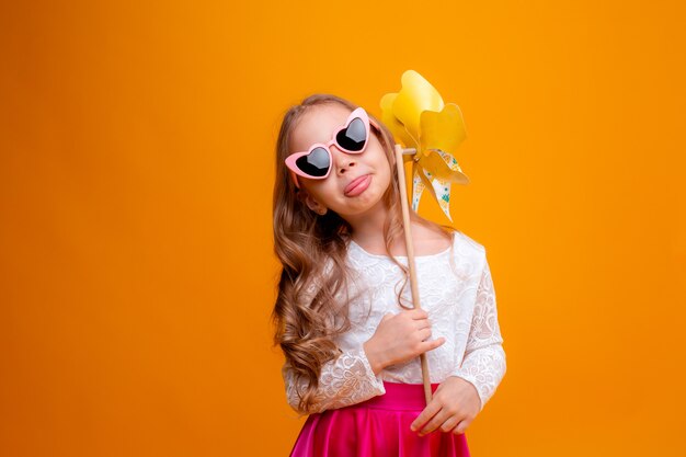 a little girl in sunglasses holds a pinwheel toy on a yellow background