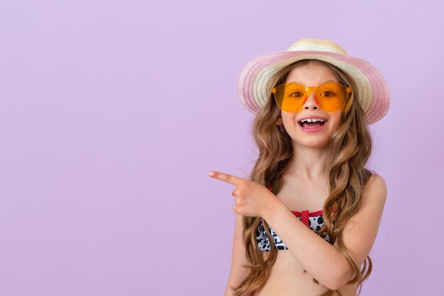 A little girl in sunglasses points a finger at your ad and smiles broadly. Copy space.