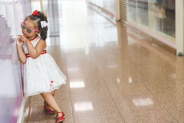 Foto la bambina in occhiali da sole sta al muro nel centro commerciale