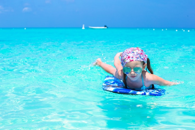 Little girl swimming on a surfboard in the turquoise sea