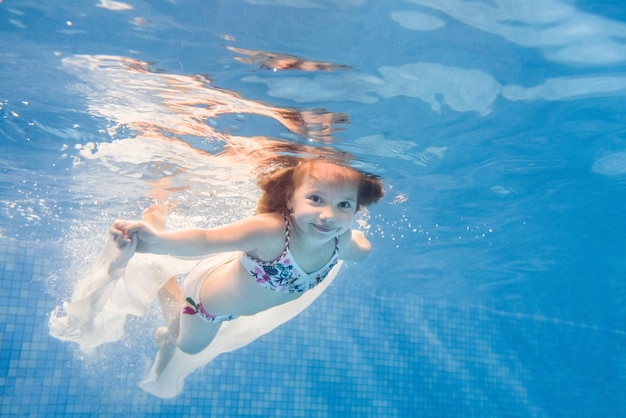 Маленькая девочка плавает под водой в детском бассейне Дайвинг учит ребенка плавать Наслаждайтесь плаванием и пузырями