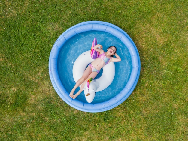 A little girl swims on an inflatable unicorn ring in an inflatable pool in the garden in summer