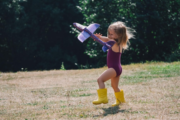 A little girl in a swimsuit laughs merrily and launches a plane into the sky summer A child runs through a clearing with an airplane Happy childhood sincere emotions Active games for kids