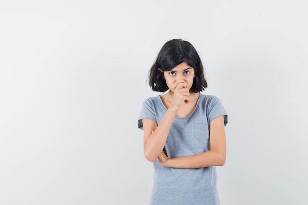 Little girl in t-shirt holding hand on chin and looking hesitant , front view.