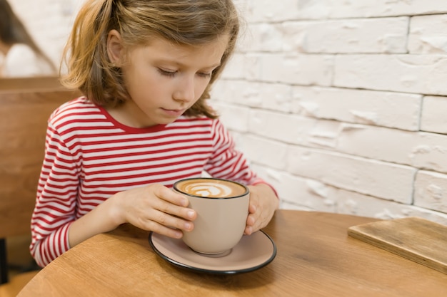 예술 음료의 큰 컵과 카페 테이블에 어린 소녀