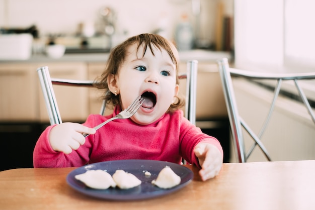 Photo little girl at  table eats dumplings on her own