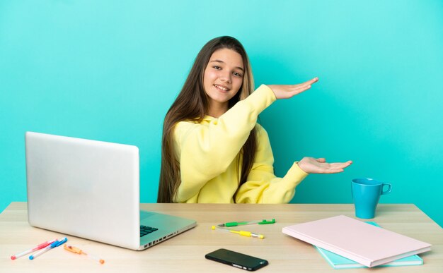 Little girl in a table with a laptop over isolated blue background holding copyspace to insert an ad