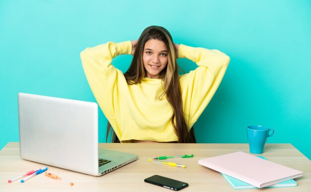 Bambina in un tavolo con un computer portatile su sfondo blu isolato ridendo