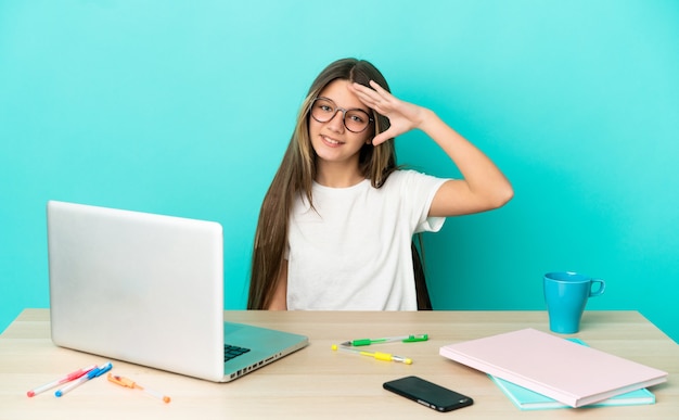 행복 한 표정으로 손으로 경례 격리 된 파란색 배경 위에 노트북 테이블에 어린 소녀