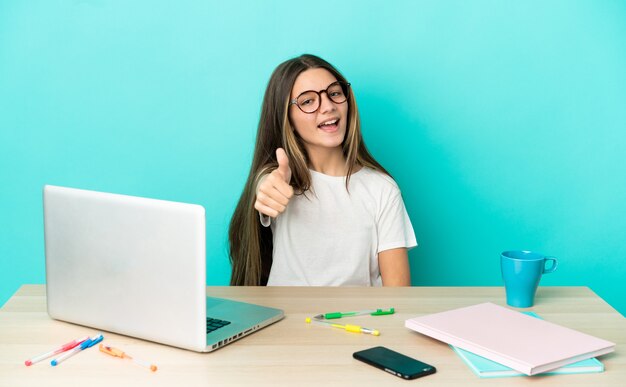 Little girl in a table with a laptop over isolated blue background with thumbs up because something good has happened