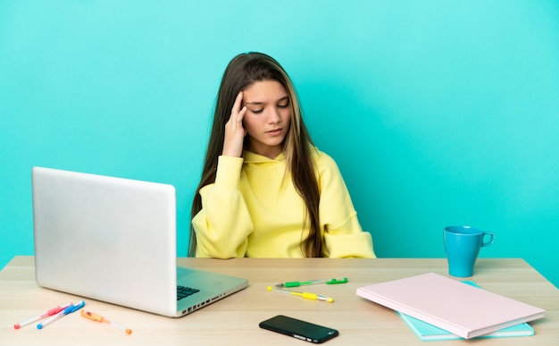 Little girl in a table with a laptop over isolated blue wall with headache