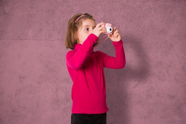 장난감 사진 카메라를 사용하여 사진을 찍는 어린 소녀