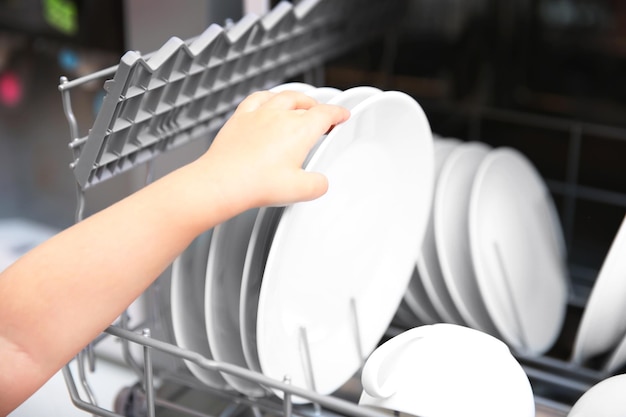 Little girl taking plates from the dishwasher closeup