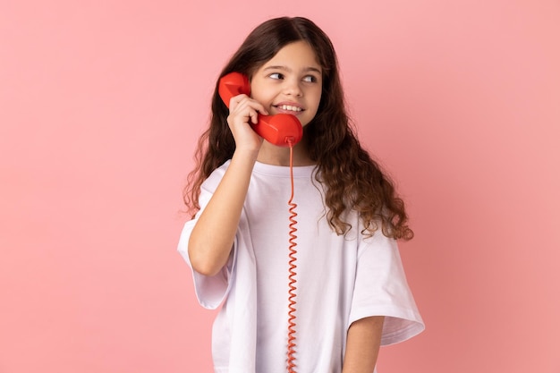 Little girl talking landline telephone holding in hand handset looking away with toothy smile