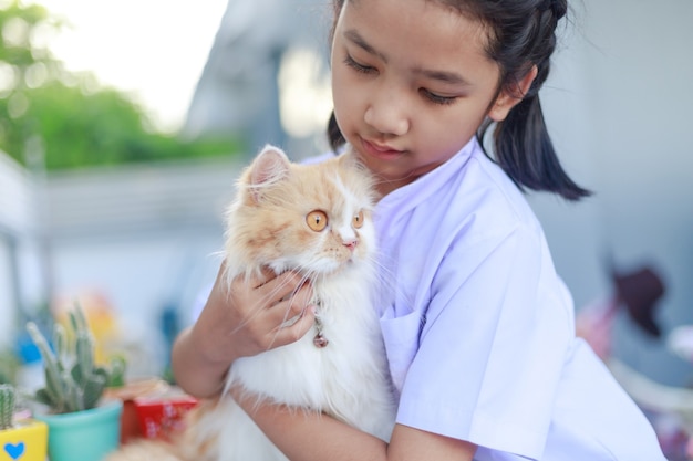 태국 학생복을 입은 어린 소녀가 페르시아 고양이를 껴안고 있다