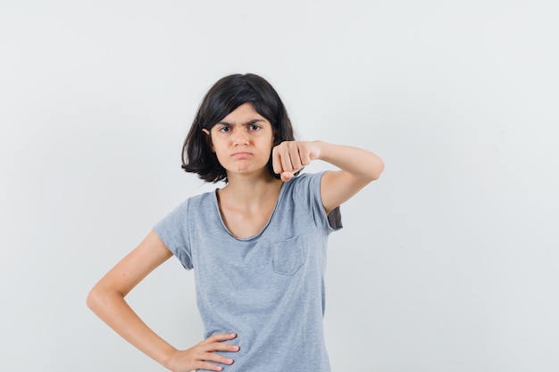 Little girl threatening with fist in t-shirt and looking spiteful. front view.