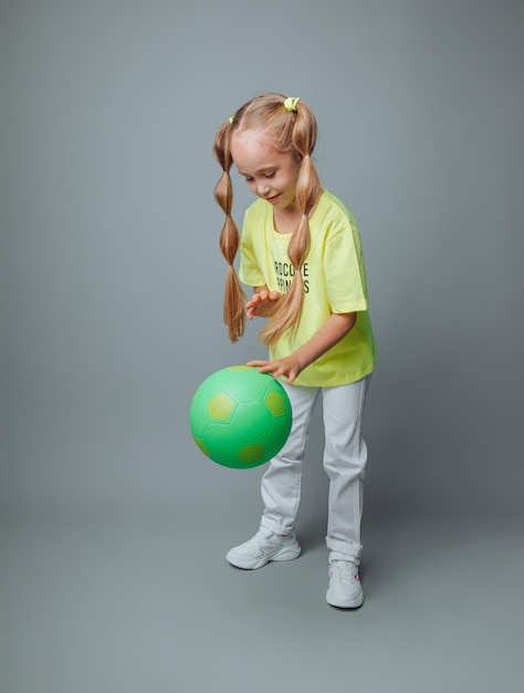 A little girl throws a ball up isolated on a gray background a little athletechildren's sports