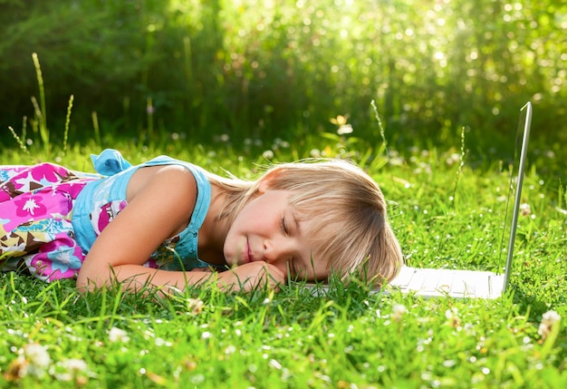 Bambina stanca di usare il laptop e si è addormentata in un giardino estivo