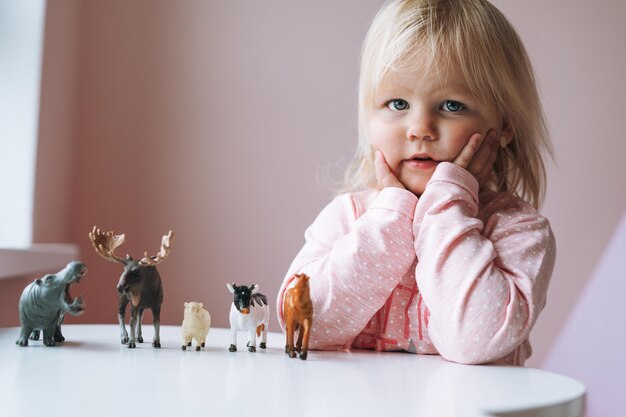 Foto piccola bambina in rosa che gioca con giocattoli per animali sul tavolo nella stanza dei bambini a casa