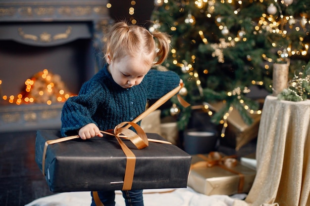 Little girl toddler standing near Christmas tree with a gift