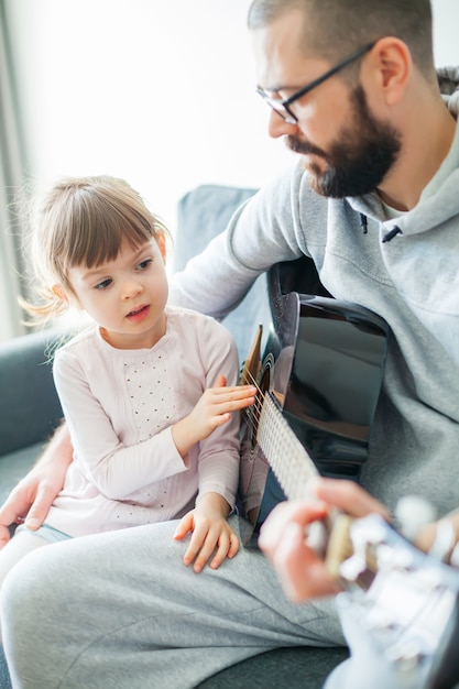 Bambina che tocca le corde della chitarra mentre suo padre suona la chitarra per lei