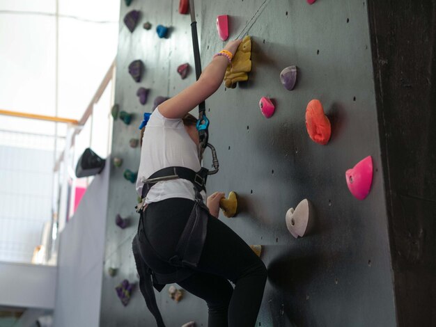 Photo a little girl trains in mountaineering climbs a wall with obstacles in a protective holding belt.