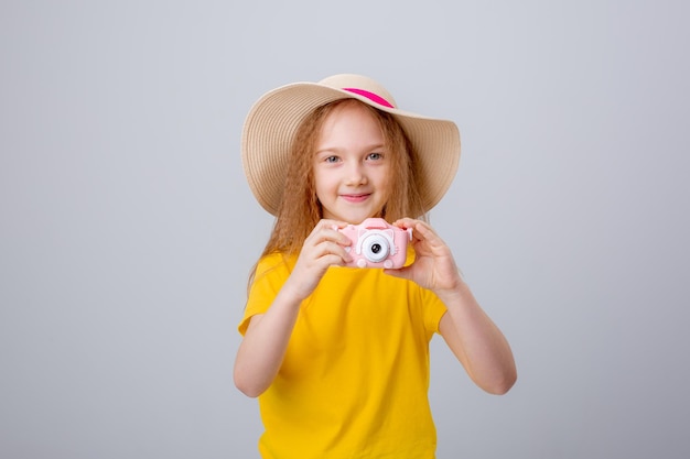 a little girl in a traveler hat holds a camera on a white background