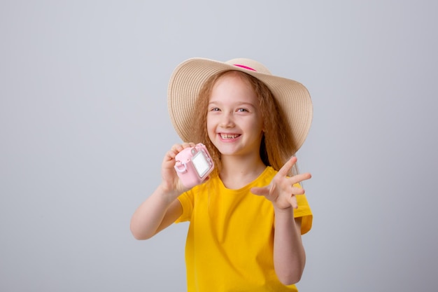 a little girl in a traveler hat holds a camera on a white background