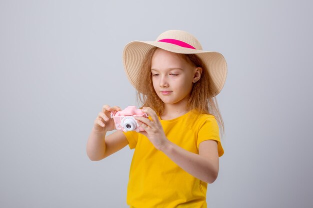 a little girl in a traveler hat holds a camera on a white background