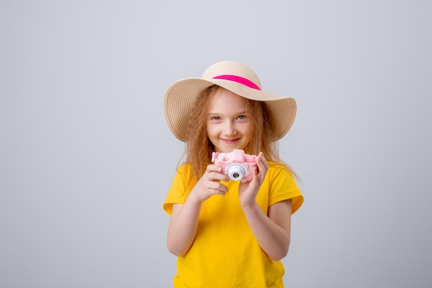 a little girl in a traveler hat holds a camera on a white background