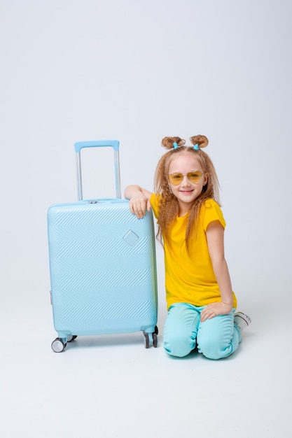 Маленькая девочка-путешественница с чемоданом на белом фоне
