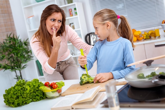 A little girl tries to cut broccoli alone and her mother is worried that she will hurt herself