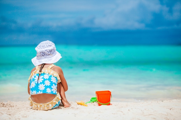 Little girl at tropical white beach making sand castle