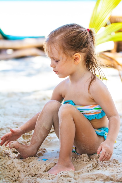 Little girl at tropical white beach making sand castle