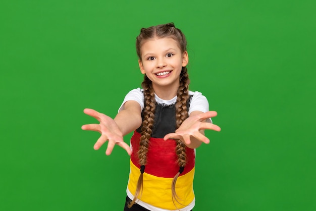 A little girl in a Tshirt with a German flag stretches her palms forward and smiles broadly against a green isolated background German language courses for schoolchildren