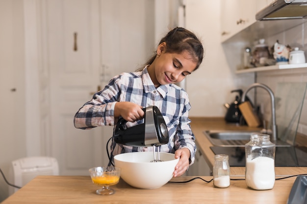 Little girl use a mixer to make a cake, skilled girl in kitchen. Child trying making cookies.