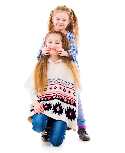 Little girl using her fingers to make her older sister smile isolated on white background